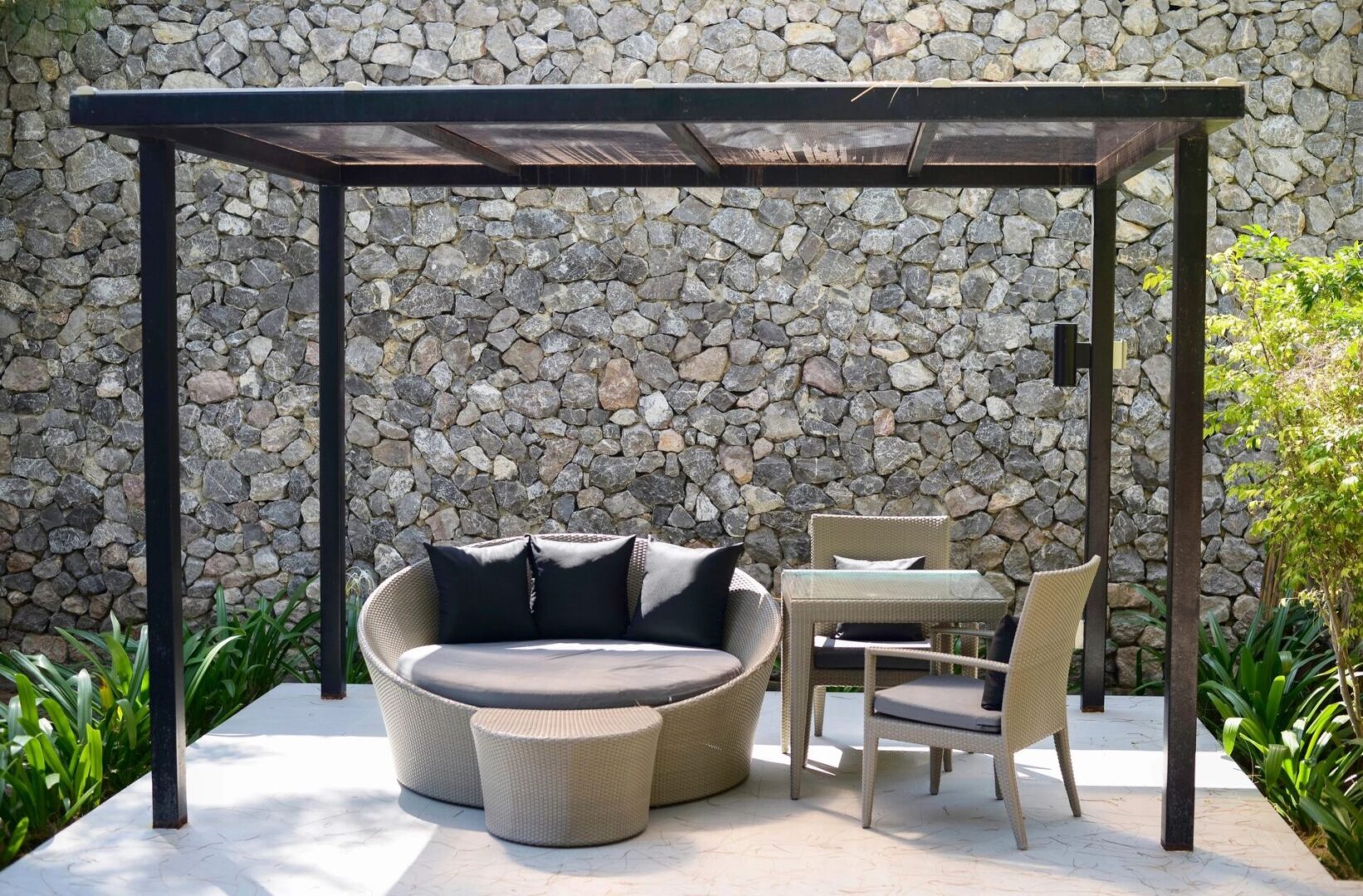 A patio with a table and chairs, couch and stone wall.