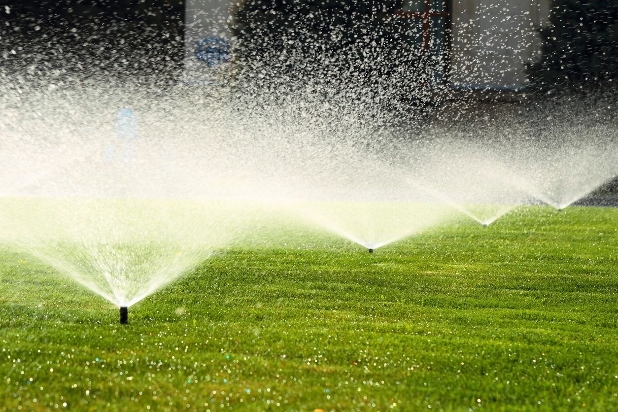 A couple of water sprinklers spraying on some grass.