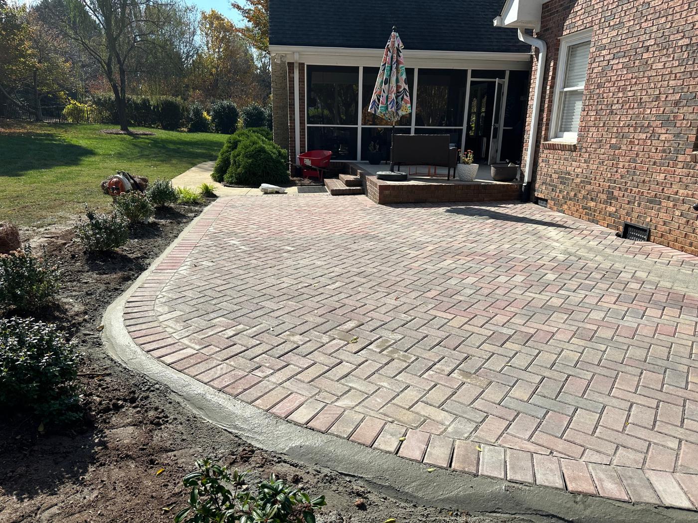 A brick patio with a fire pit and flower bed.