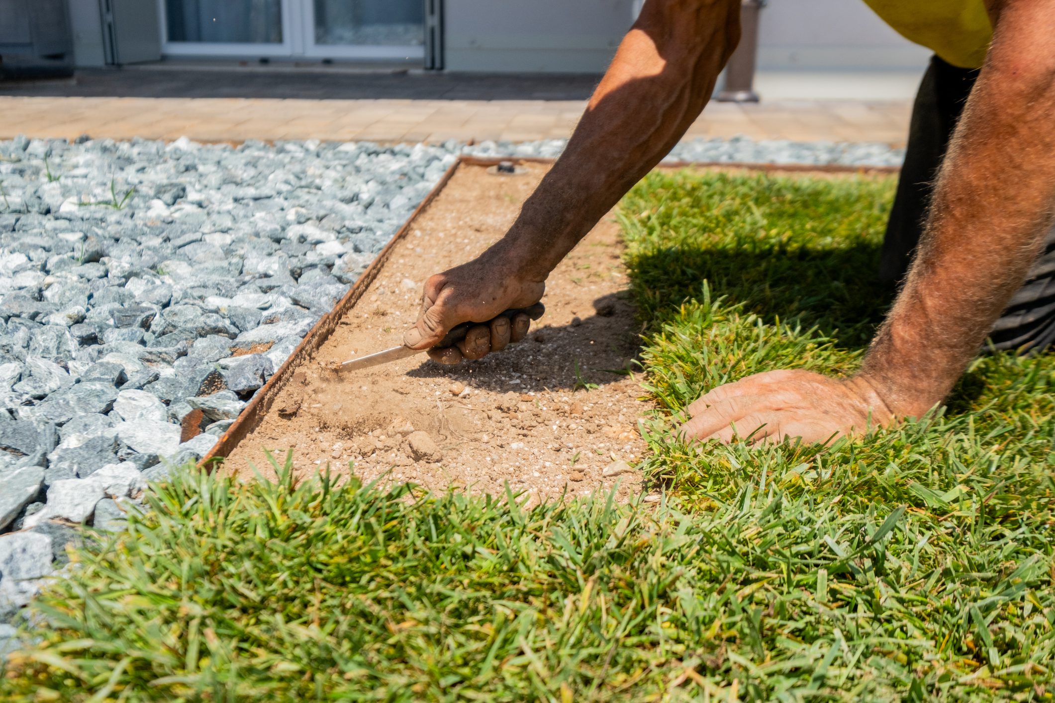 Close-up of a worker manually adjusting turf next to gravel using a knife. Ideal for landscaping, gardening, home improvement, or DIY concepts
